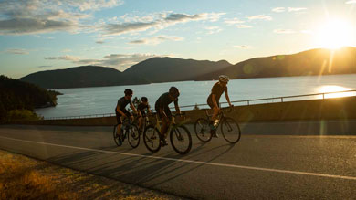 Group of cyclists riding on a road by a lake during sunset