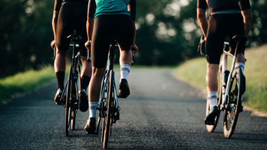 Three cyclists riding on a road surrounded by greenery on a sunny day