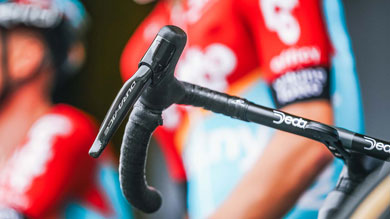 Close-up of a bicycle handlebar with cyclists in red jerseys in the background