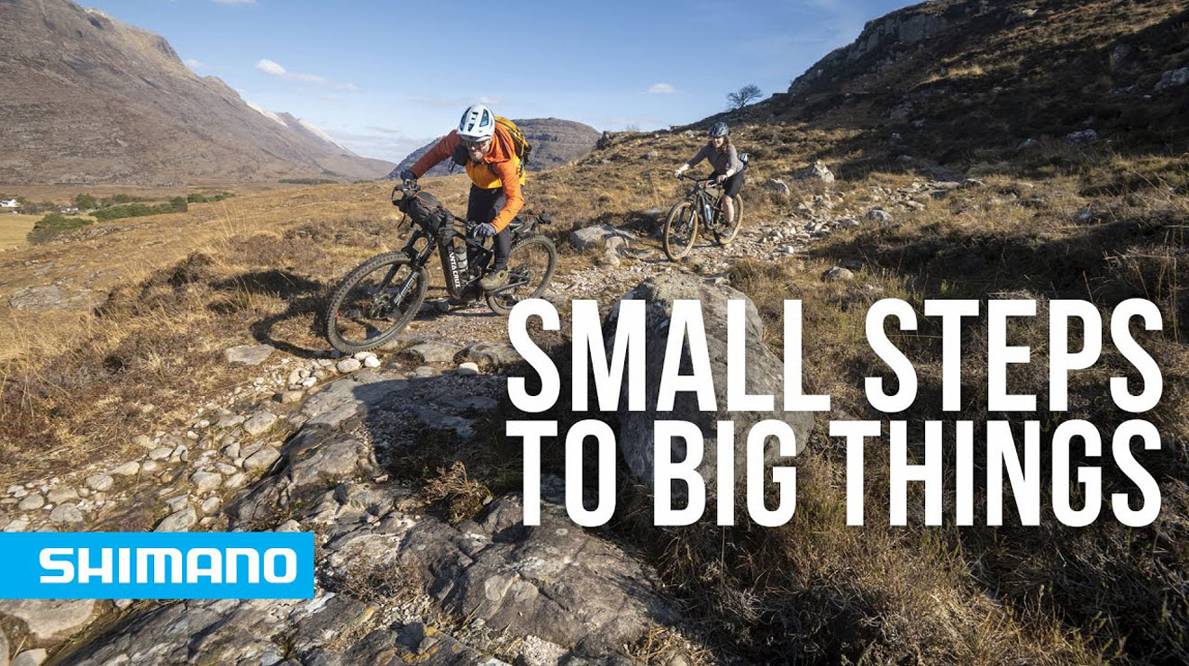Two cyclists riding on a rocky trail through a mountainous landscape