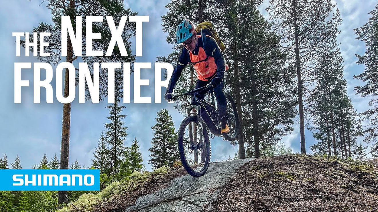 Mountain biker riding downhill with 'The Next Frontier' text and Shimano logo