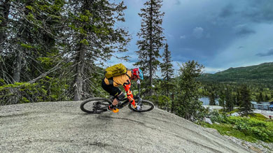 Person mountain biking on a steep trail surrounded by trees and mountains