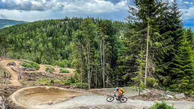 Mountain biker riding on a forest trail with lush green trees and cloudy sky