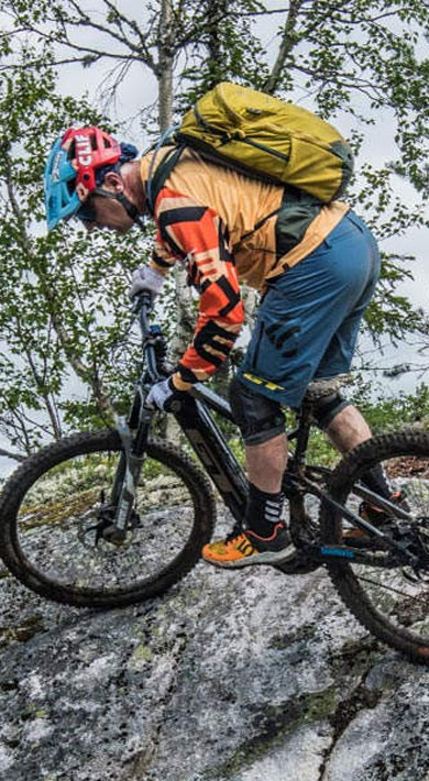 Mountain biker navigating rocky terrain in a forested area under cloudy skies