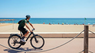 Person riding a bike along the beach with people in the background under umbrellas