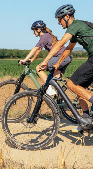 Two people cycling on a dirt path through a rural landscape.
