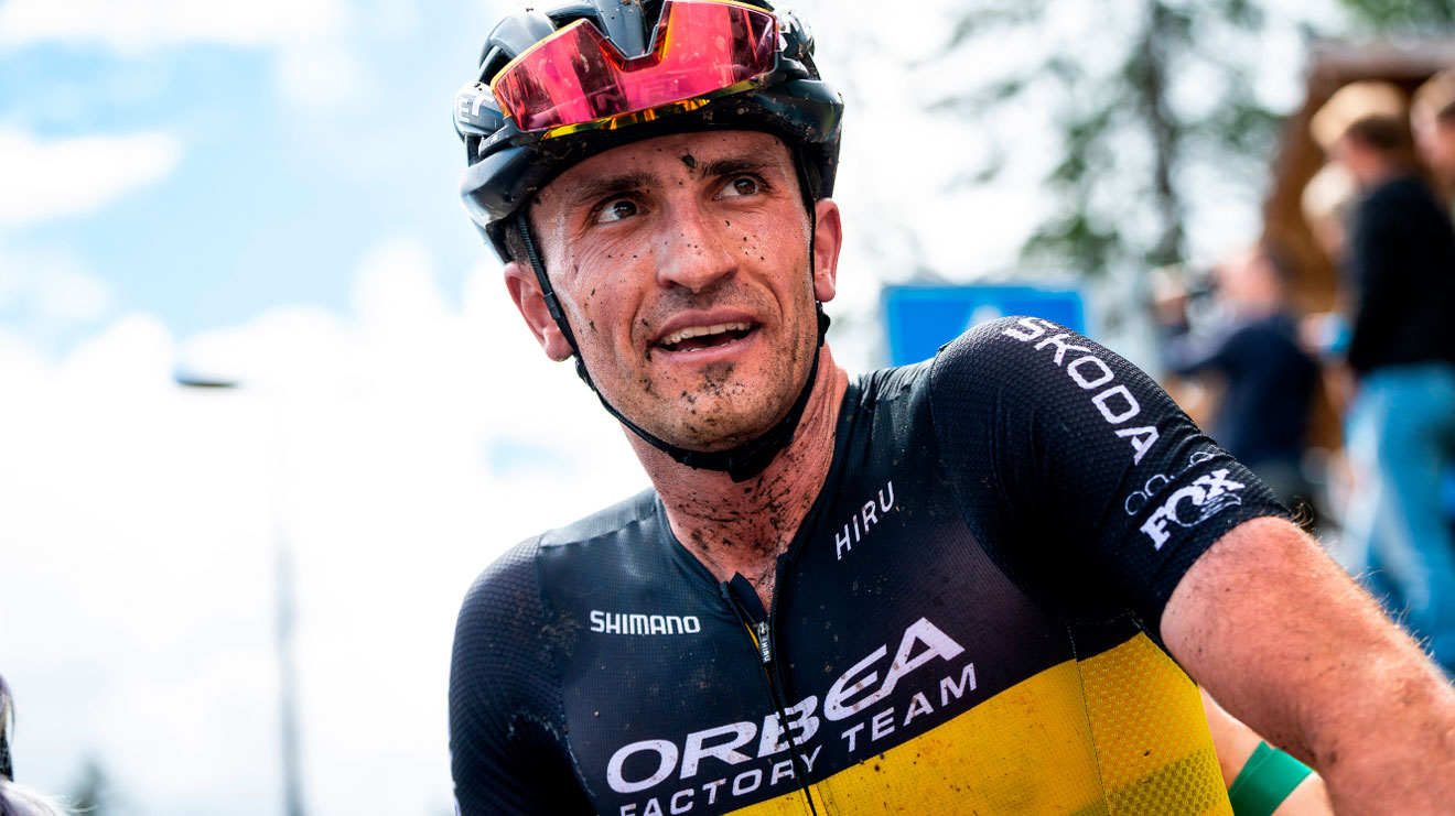 Cyclist in Orbea Factory Team gear looking to the right, with dirt on his face and helmet