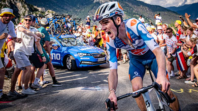 Cyclist climbing a mountain road surrounded by cheering fans and support vehicle in a cycling race