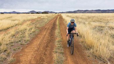 Cyclist riding on a dirt trail through a dry grassy field with mountains in the background