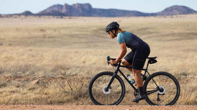 Cyclist riding on a gravel path through a vast open field with mountains in the background
