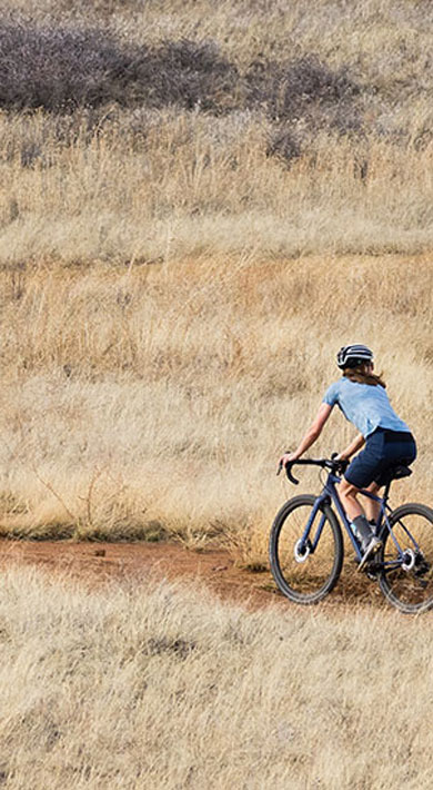 Two cyclists riding on a winding dirt path through dry grasslands