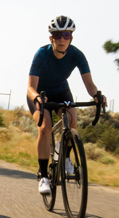 Two cyclists riding on a scenic road with trees and hills in the background