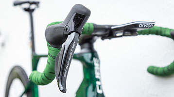 Gros plan du guidon et du levier de changements de vitesse d'un vélo avec ruban de cintre vert et inscription "Dura-Ace" et "Cube"