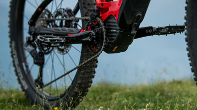 Close-up of a mountain bike resting on a grassy field, with focus on the pedal and drivetrain.